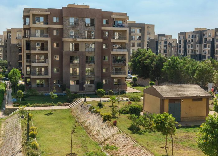 A scenic view of a modern apartment complex surrounded by greenery under a clear blue sky.
